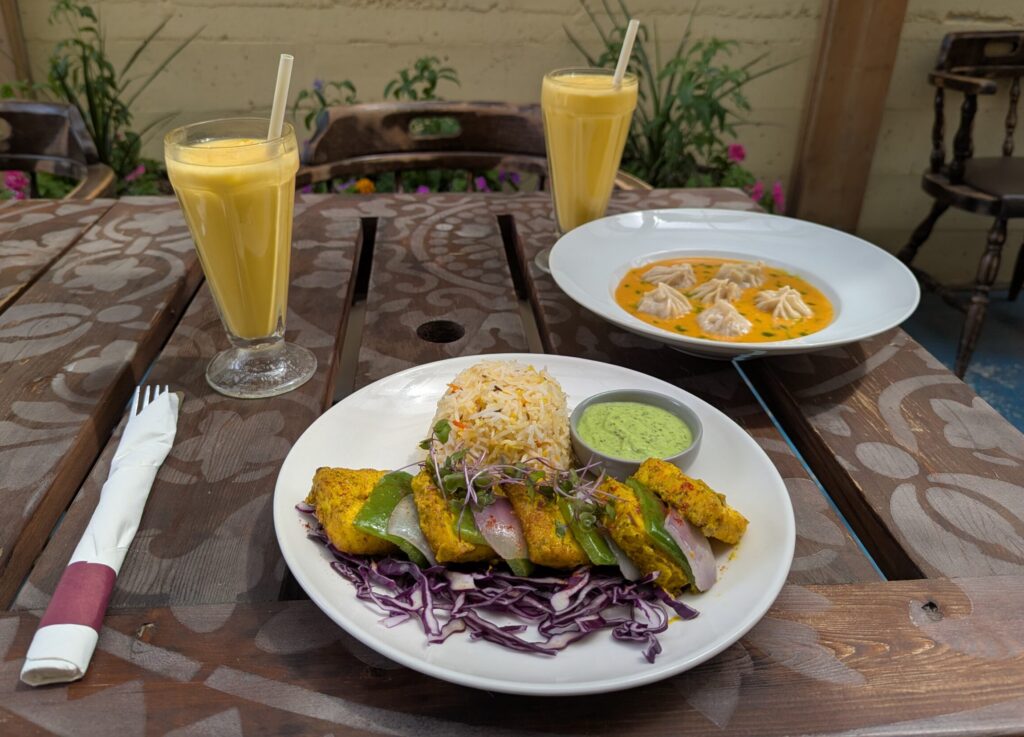 Table setting with mango drinks, a plate of paneer with saffron rice and a bowl of steamed momos.